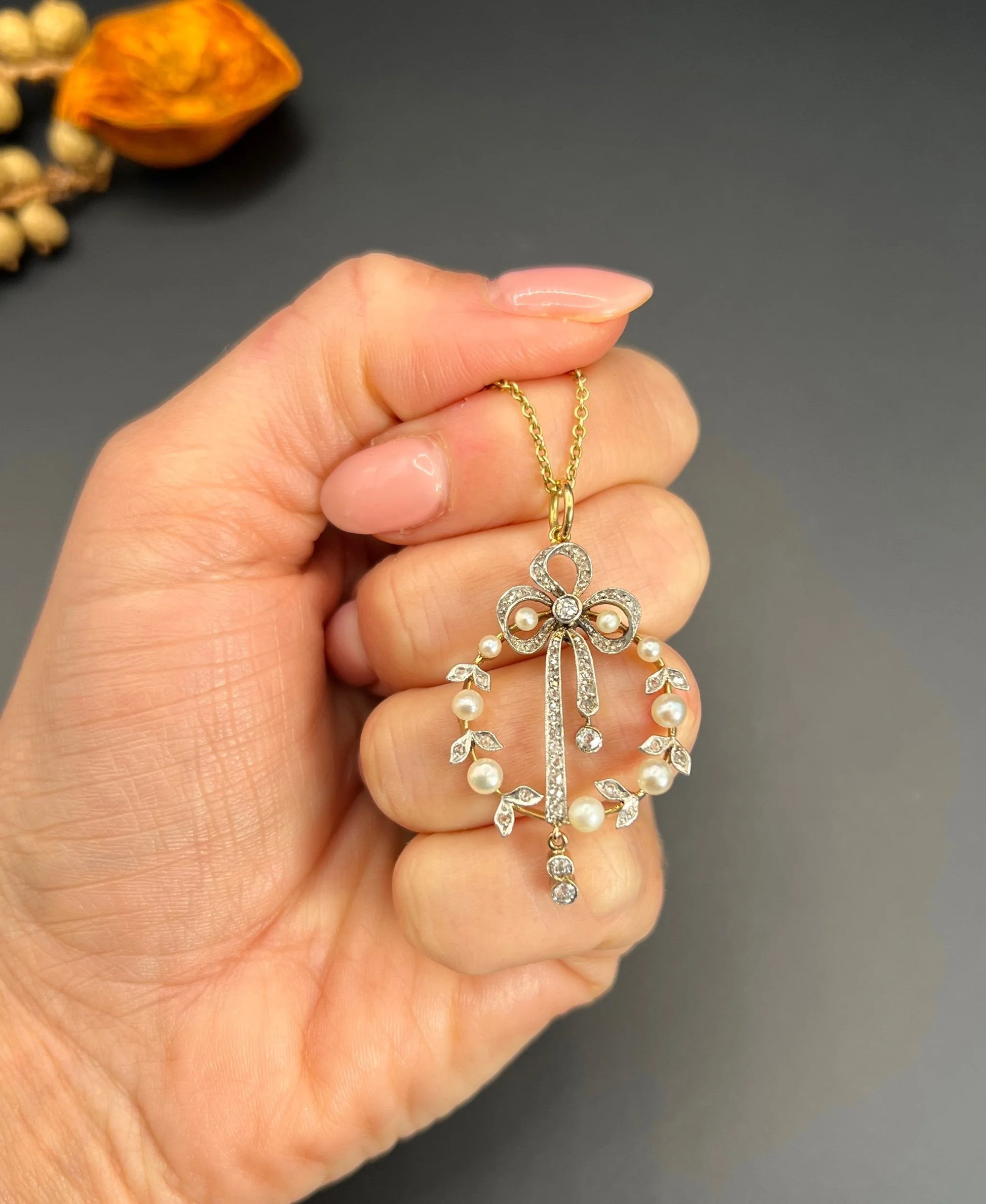 A pearl and diamond bow pendant in gold and platinum, with a chain, held in a hand
