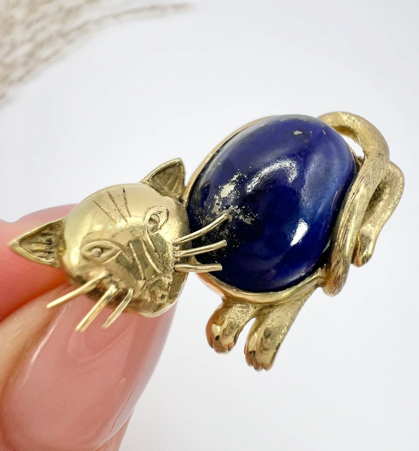 A yellow gold cat brooch with a lapis lazuli body, held in a hand