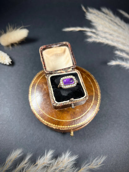 A cabochon amethyst and pearl halo cluster ring in gold, in a ring box