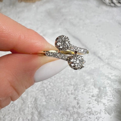 A two stone diamond crossover ring in yellow and white gold, held in a hand