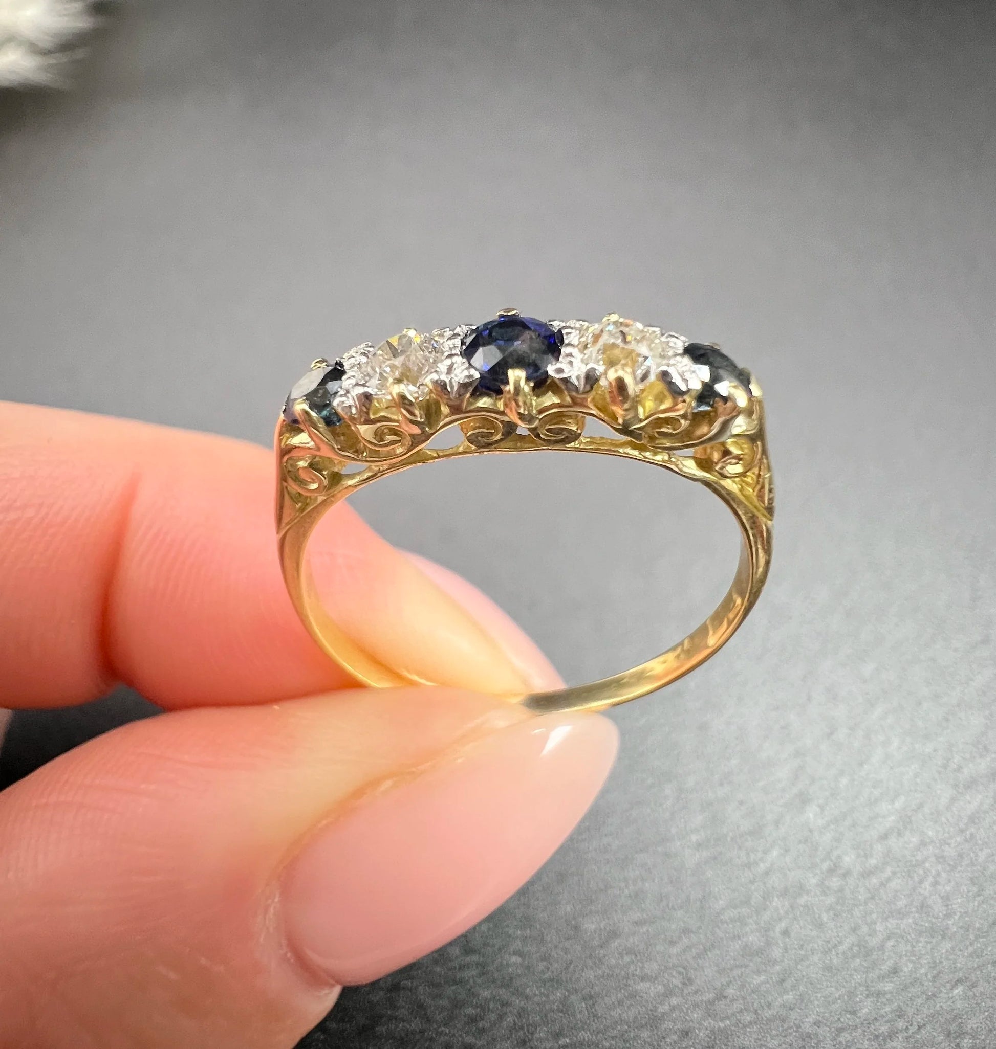 A yellow gold five stone sapphire and diamond carved half hoop ring, held in a hand
