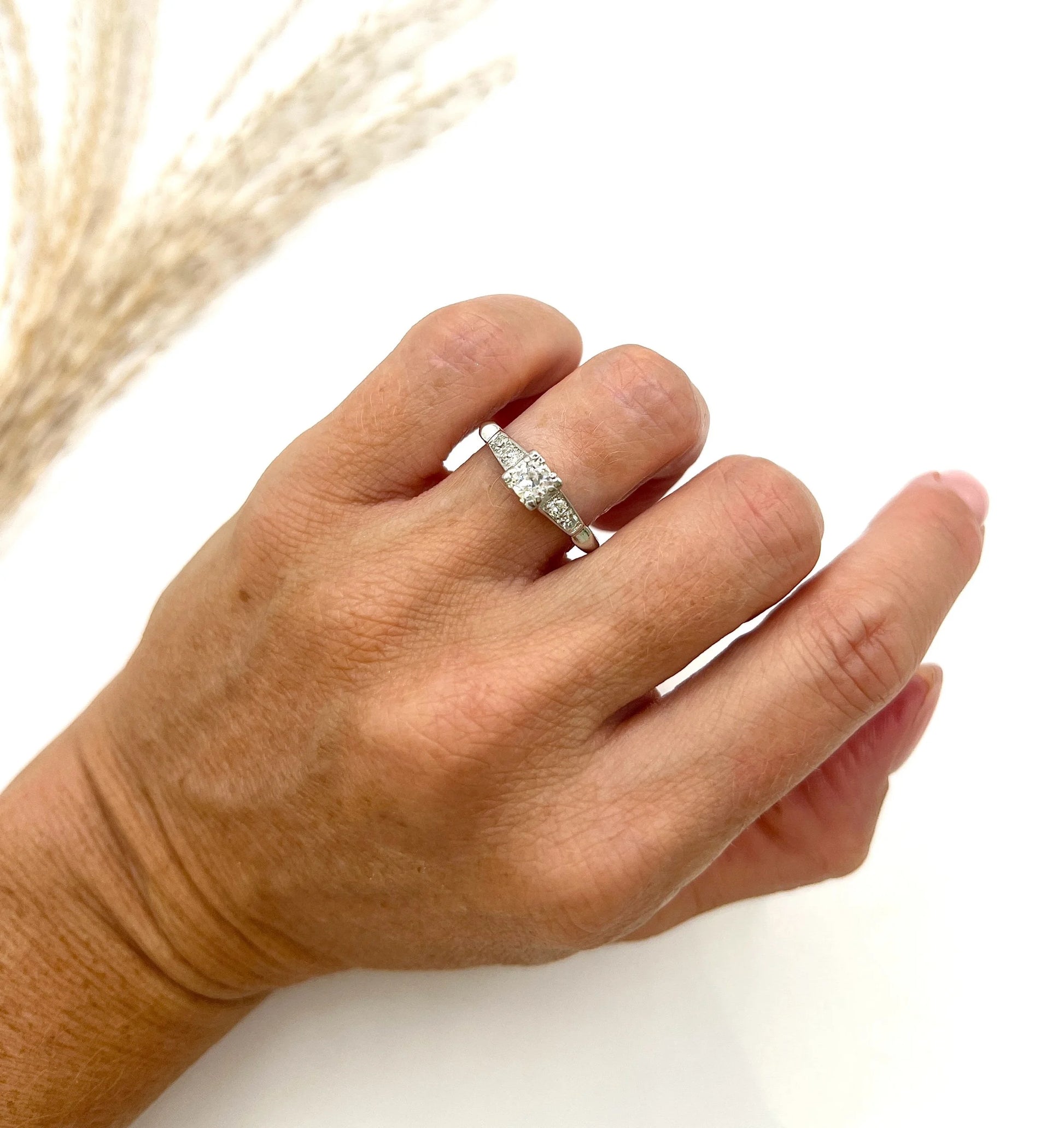 A solitaire diamond ring in platinum, with diamond set shoulders, modelled on a hand