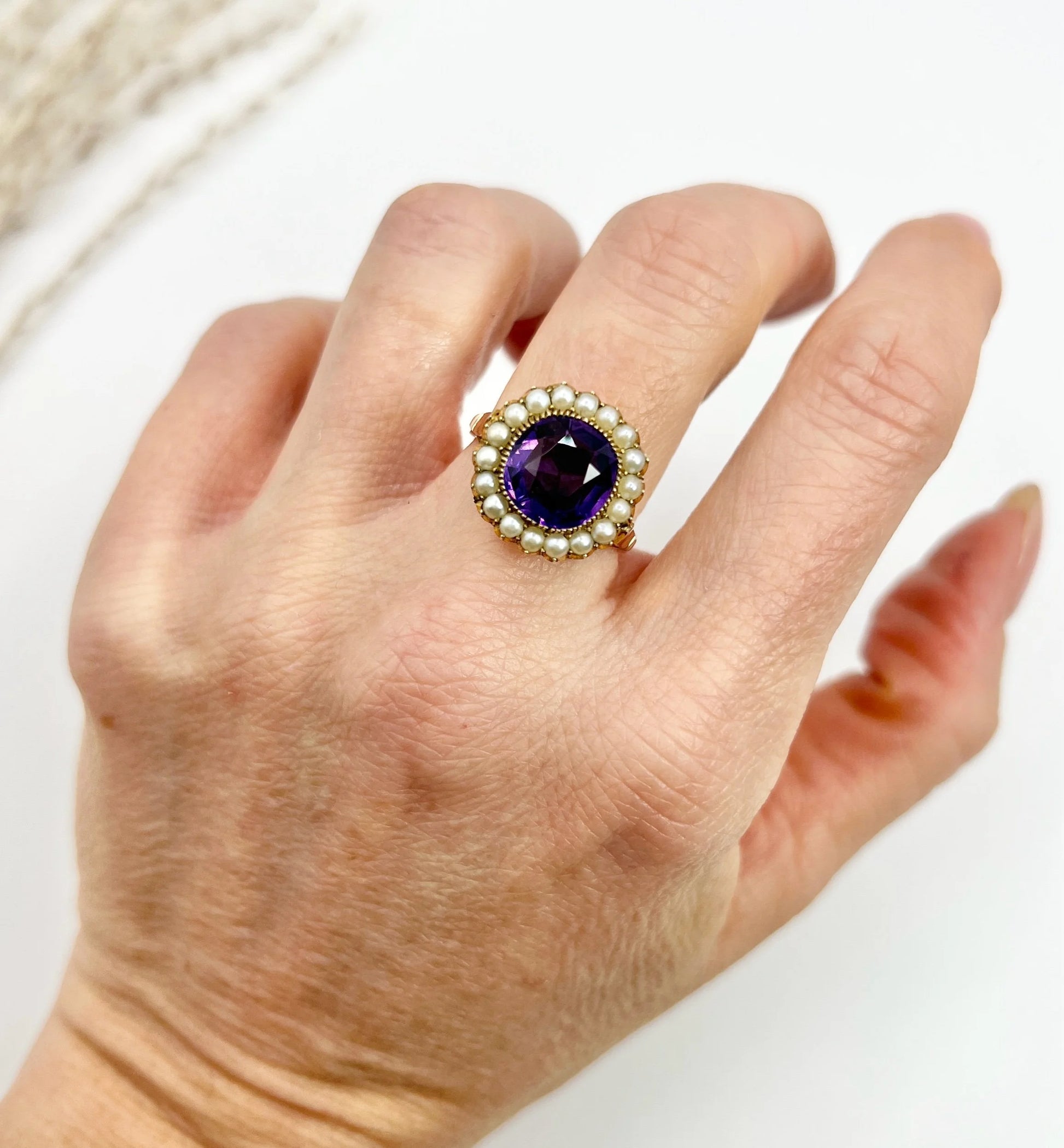 A cushion shaped amethyst cluster ring with a pearl border, in yellow gold, modelled on a hand