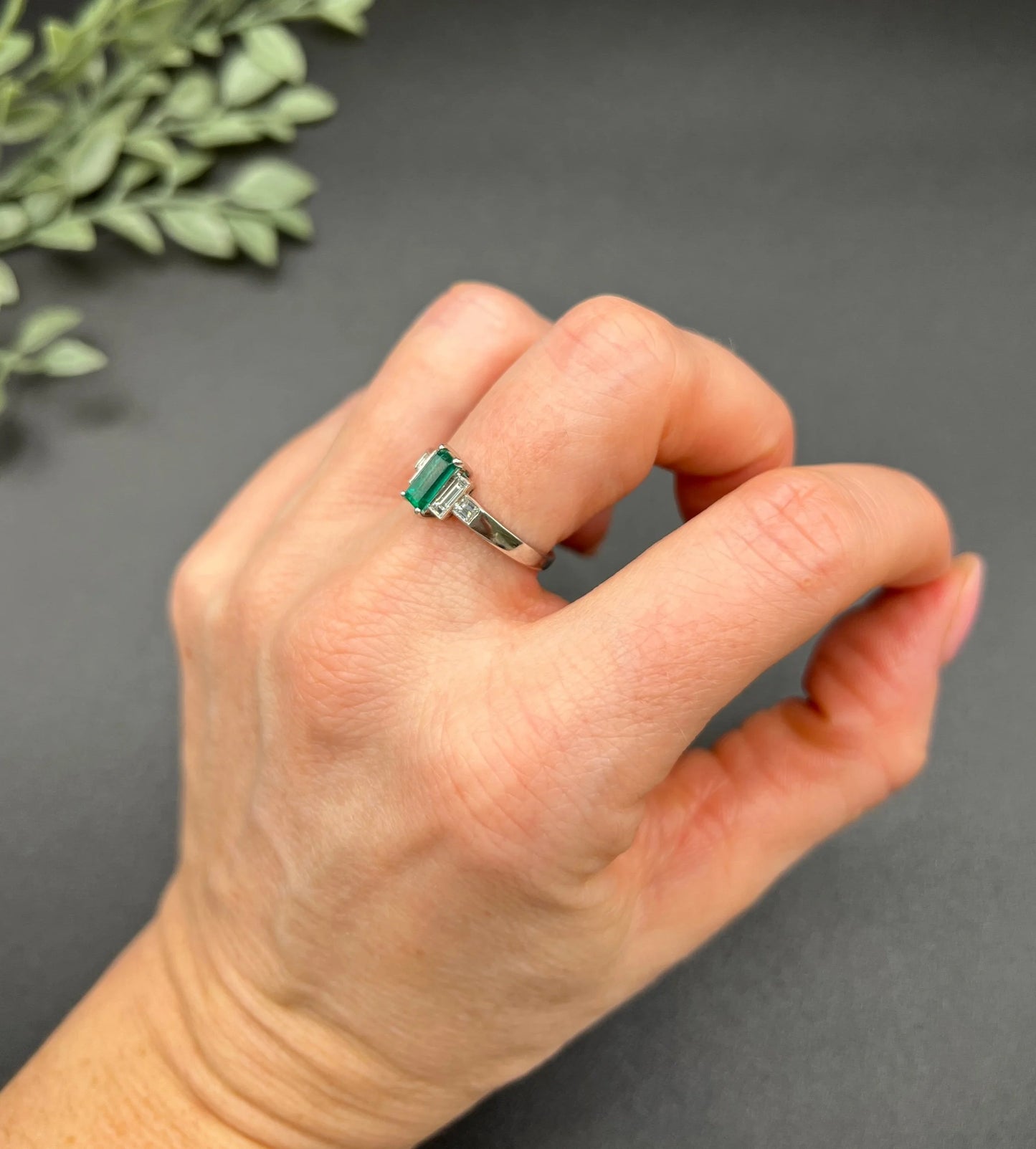 A five stone emerald cut emerald and baguette and square cut diamond ring in platinum, modelled on a hand