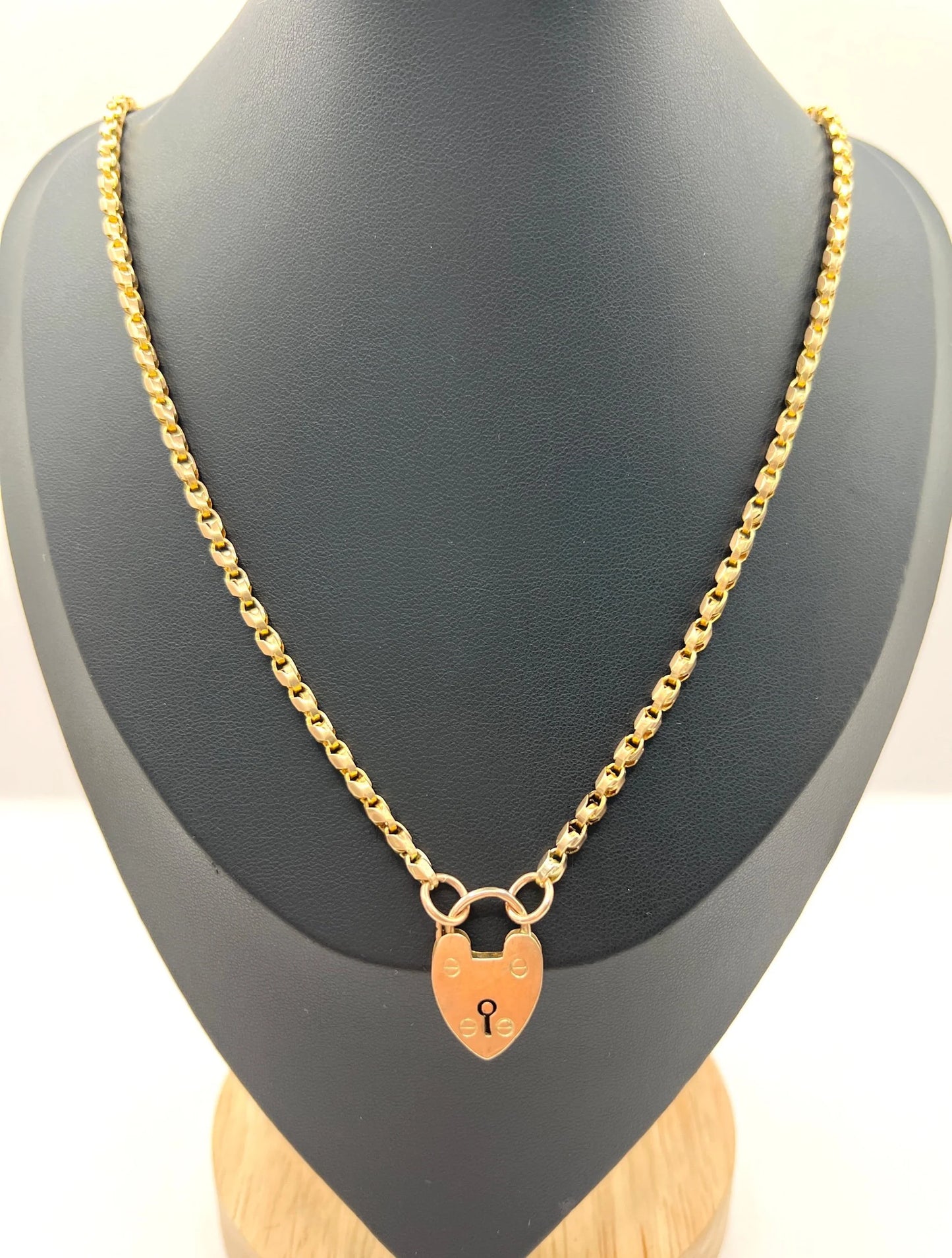 A gold chain necklace withgold heart padlock, modelled on a black bust