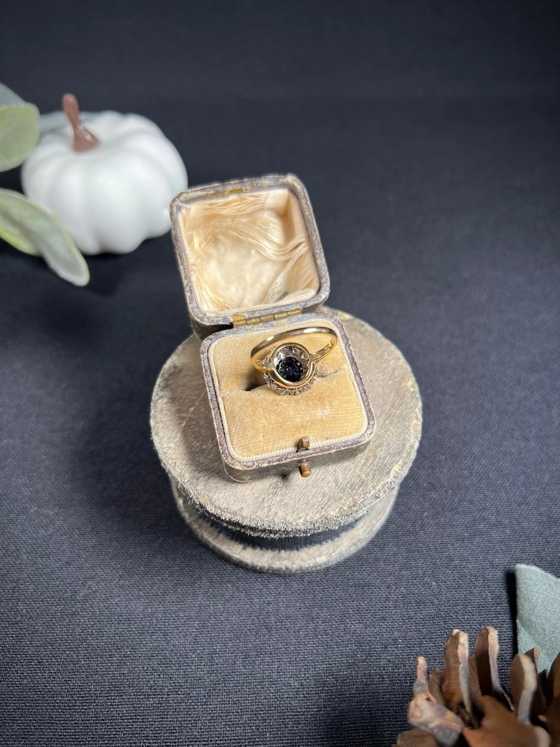 A round sapphire and diamond cluster ring, in an antique ring box