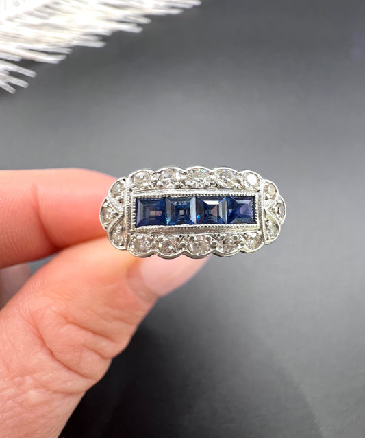 A sapphire and diamond elongated cluster ring in platinum and yellow gold, held in a hand