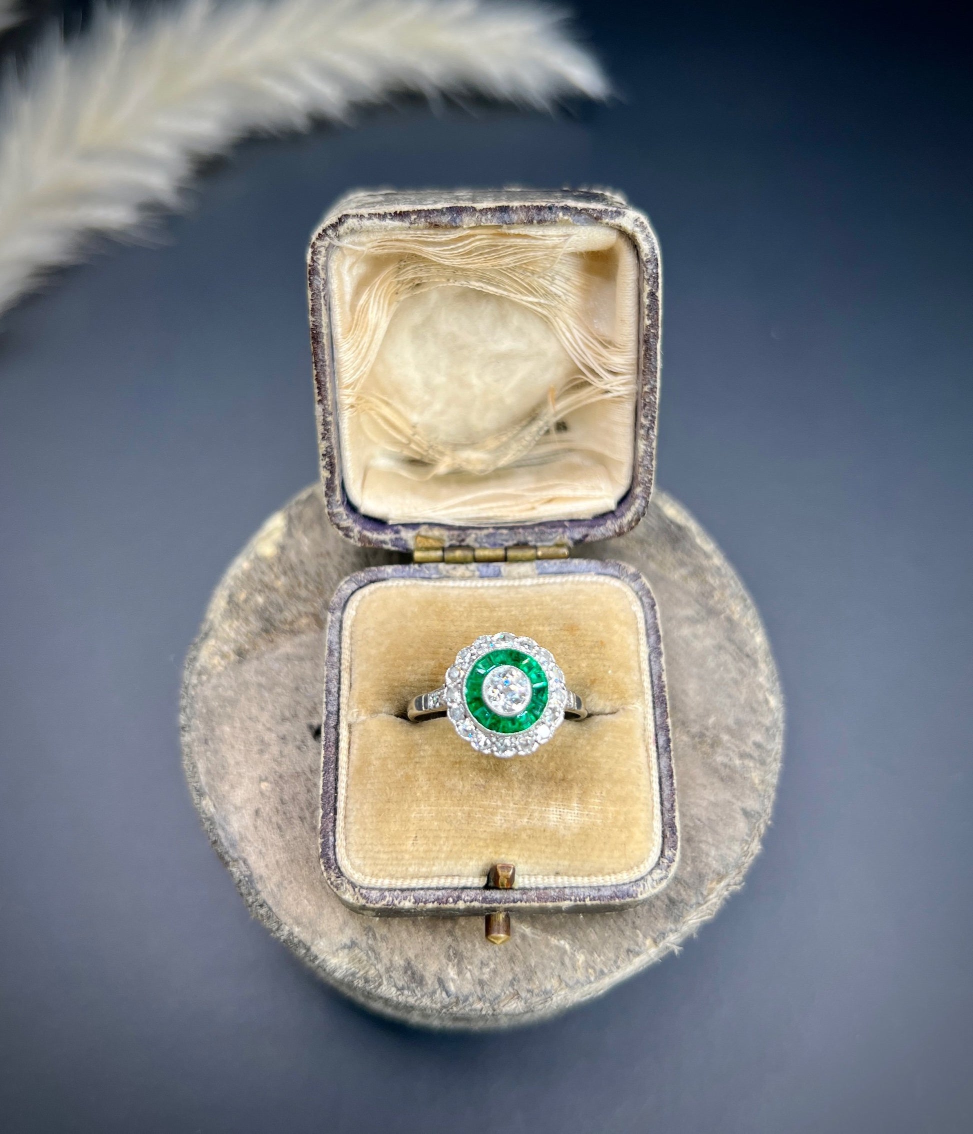 An emerald and diamond target cluster ring in platinum, in a ring box