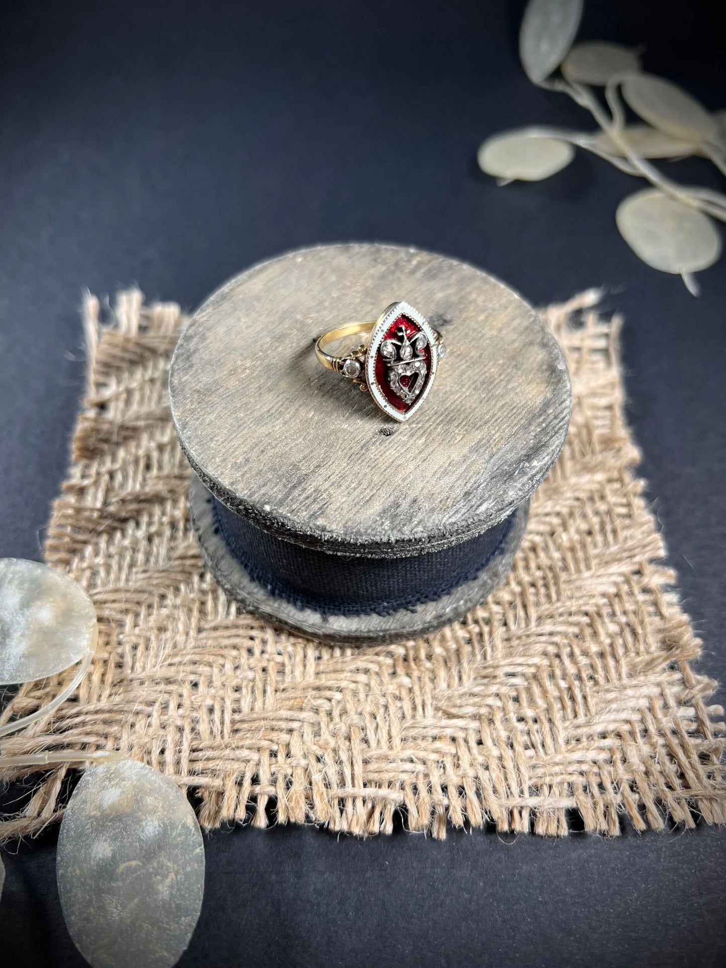 An ornate diamond and enamel navette shaped antique ring, on a wooden spool