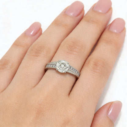 A brilliant cut diamond solitaire ring with square diamond set shoulders, in platinum, modelled on a hand