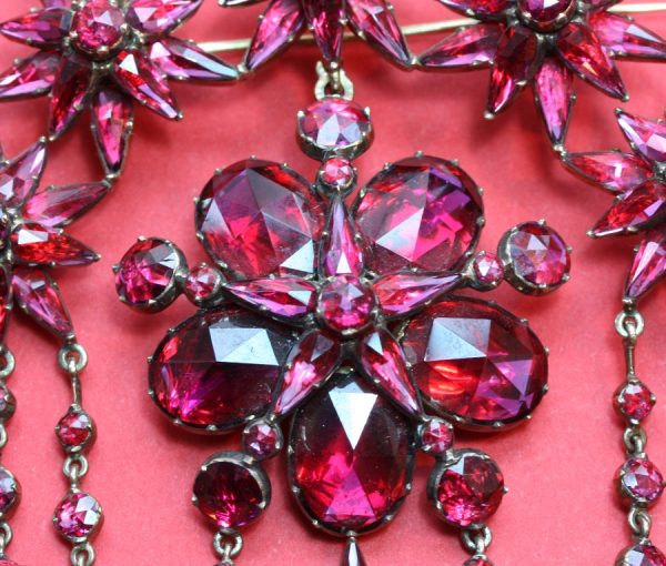 Antique Georgian Garnet and 18ct Gold Demi Suite; star earrings, cross pendant and large devant de corsage brooch, set with rose-cut garnets, Circa 1865.