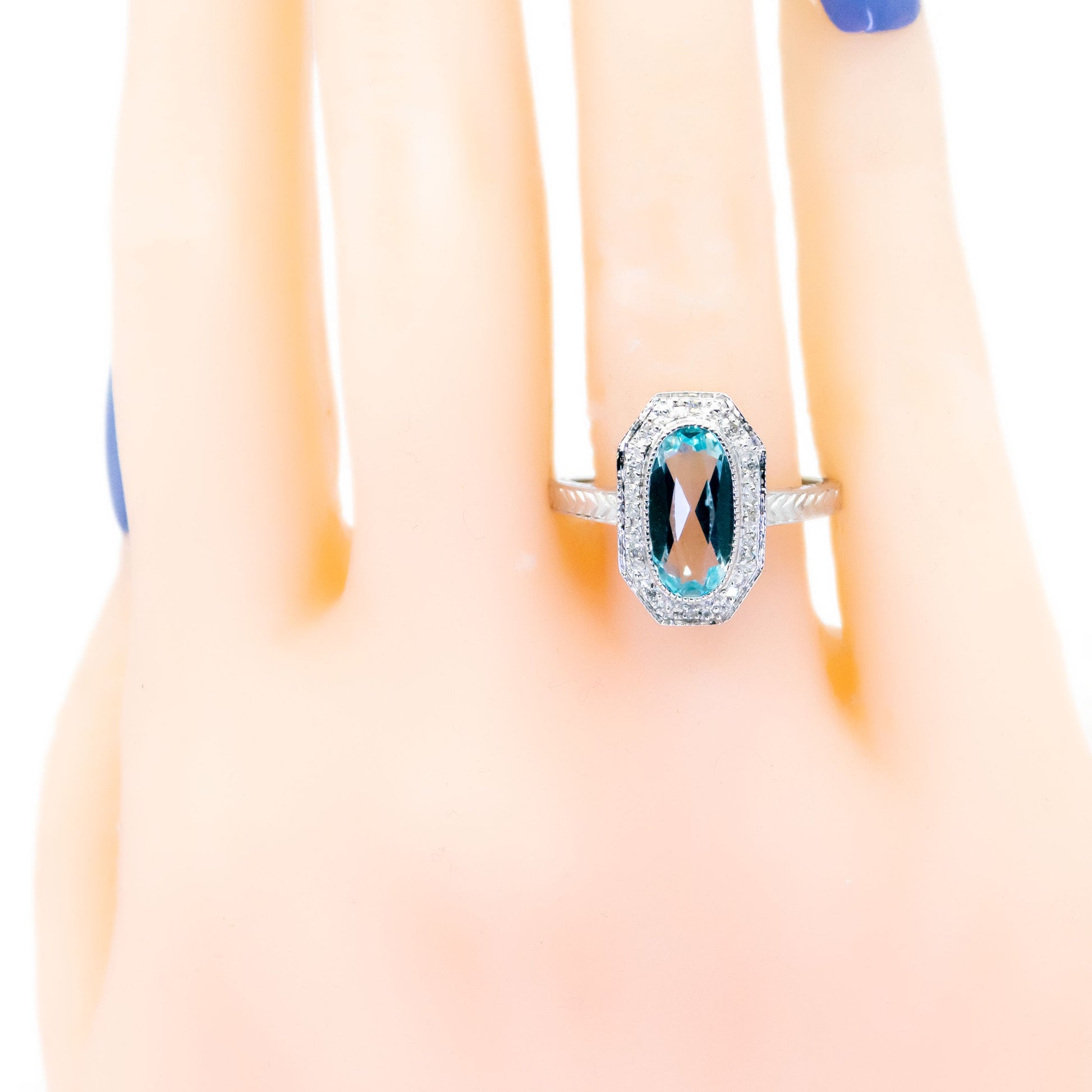 An oval blue topaz and diamond dress ring in white gold, modelled on a hand