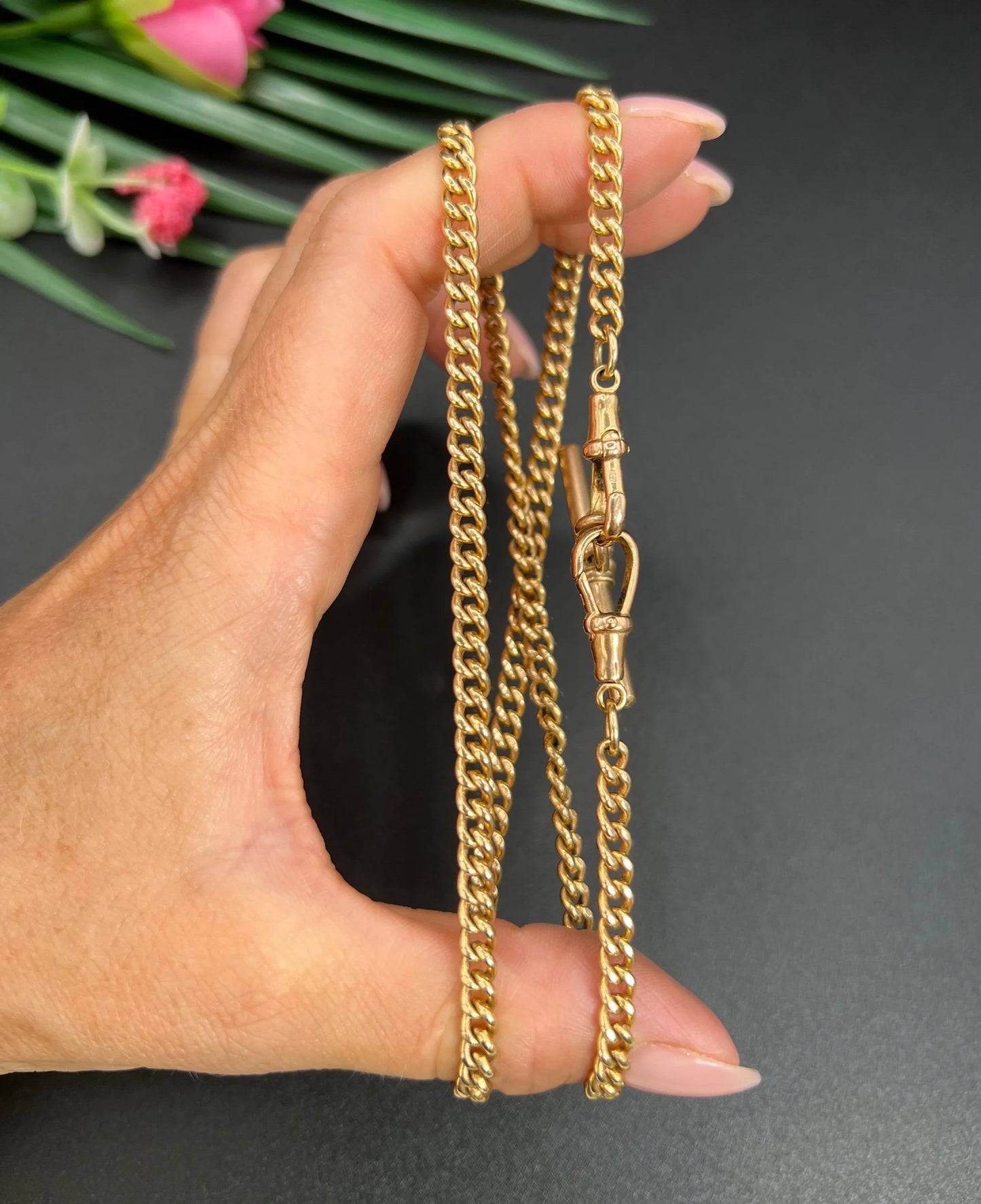 A gold curb link Albert chain, held in a hand