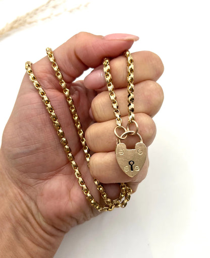 A gold chain necklace with gold heart padlock, held in a hand