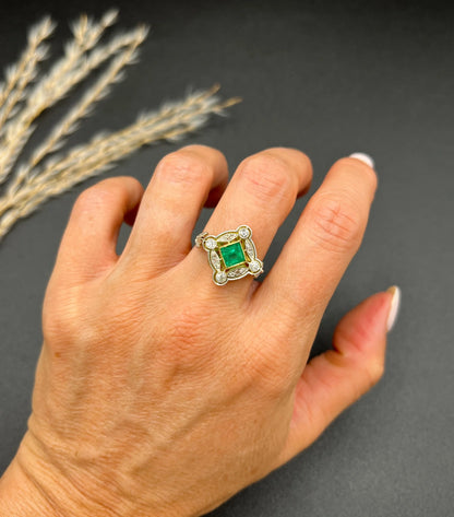 A gold and platinum ring with a centre emerald and diamond surround, modelled on a hand