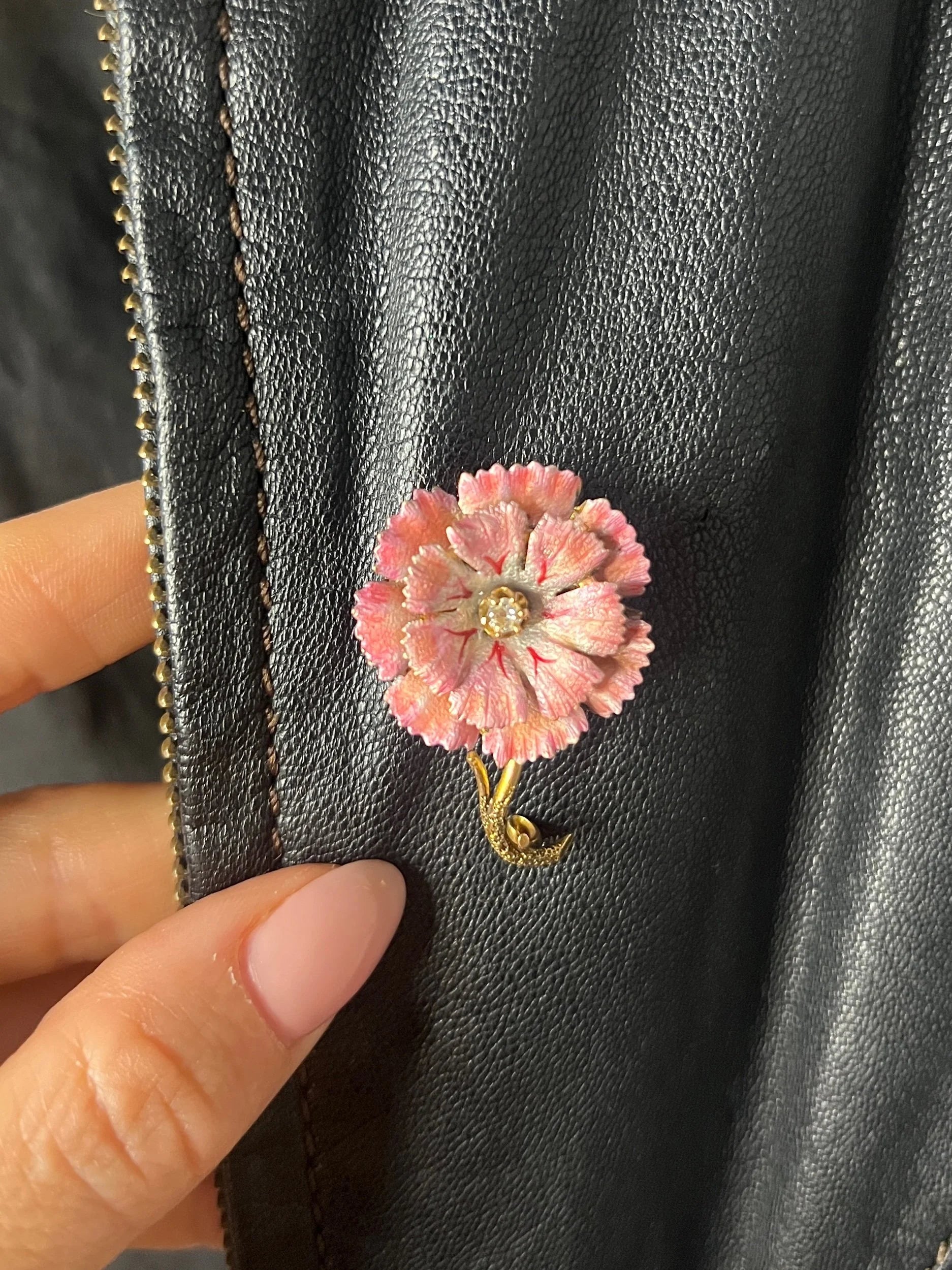 A pink enamelled flower brooch with a diamond centre, in yellow gold, on a black leather jacket