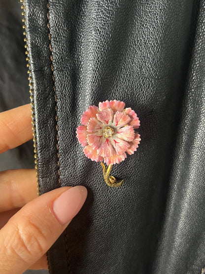 A pink enamelled flower brooch with a diamond centre, in yellow gold, on a black leather jacket