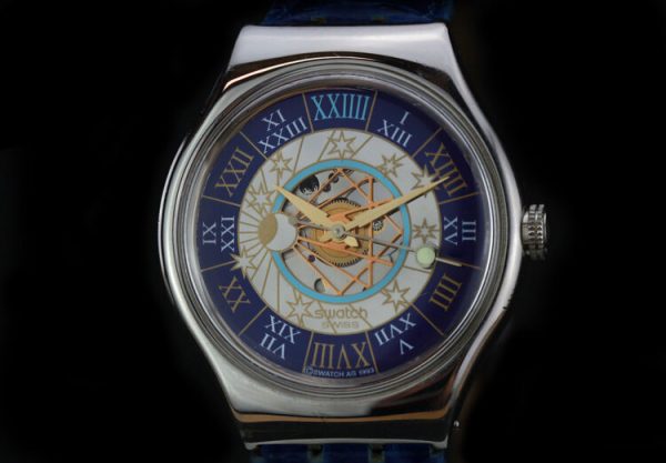 Swatch Tresor Magique Platinum 36mm Automatic Wrist Watch, golden face with celestial detailing, Roman numeral markers on outer blue band, blue leather strap, Circa 2000's