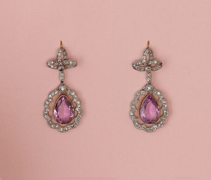 Antique Edwardian Pink Topaz and Diamond Cluster Drop Earrings; pear-cut faceted pink topaz within rose-cut diamond set surround suspended from bows set with rose cut diamonds, mounted in platinum and backed with gold. England, circa 1910