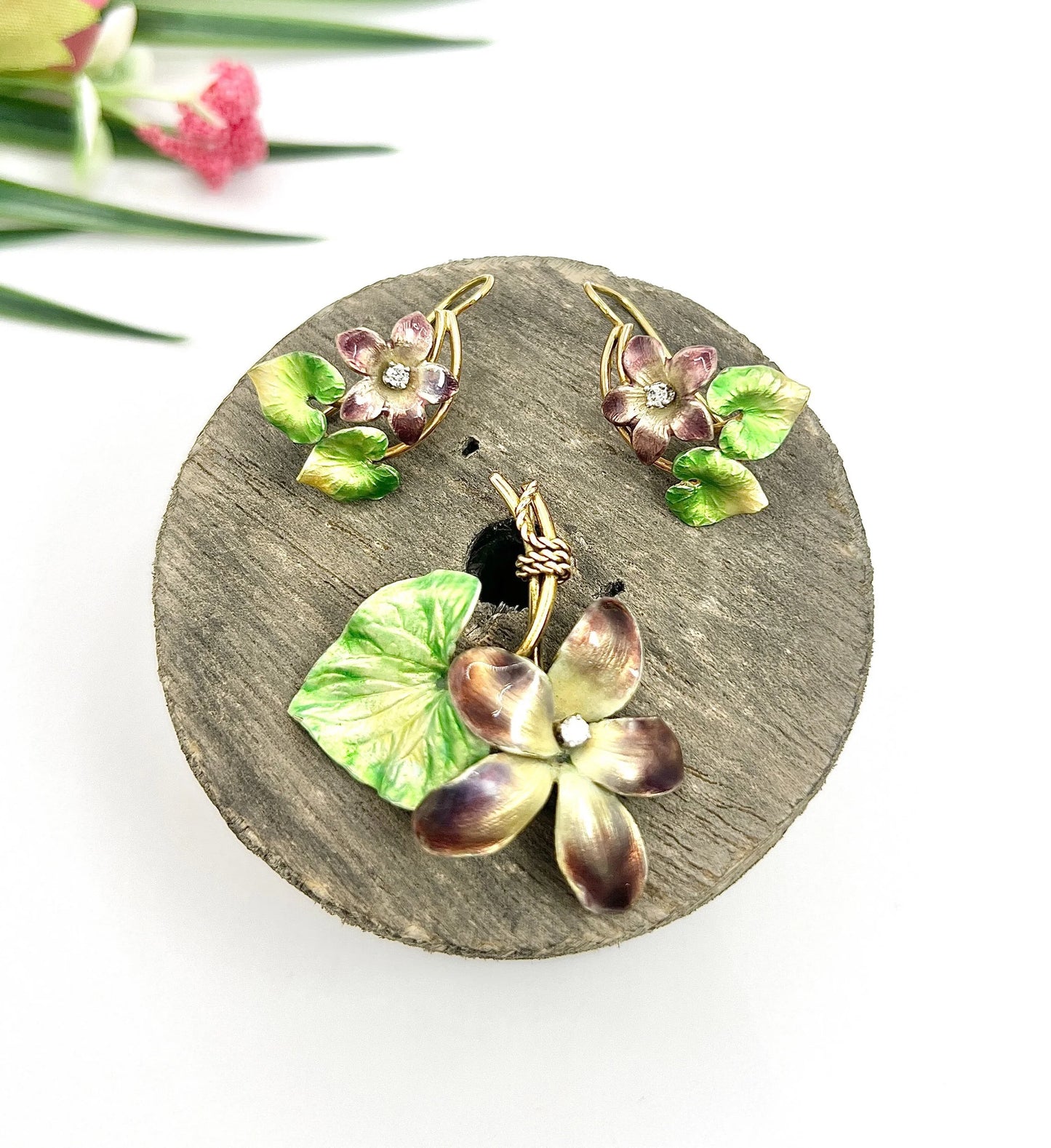 An enamelled flower suite comprising pendant and earrings, sitting on top of a wooden object