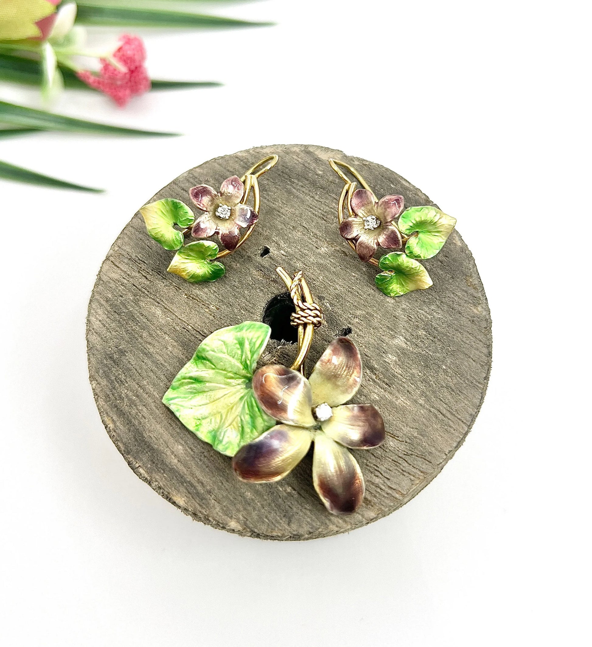 An enamelled flower suite comprising pendant and earrings, sitting on top of a wooden object