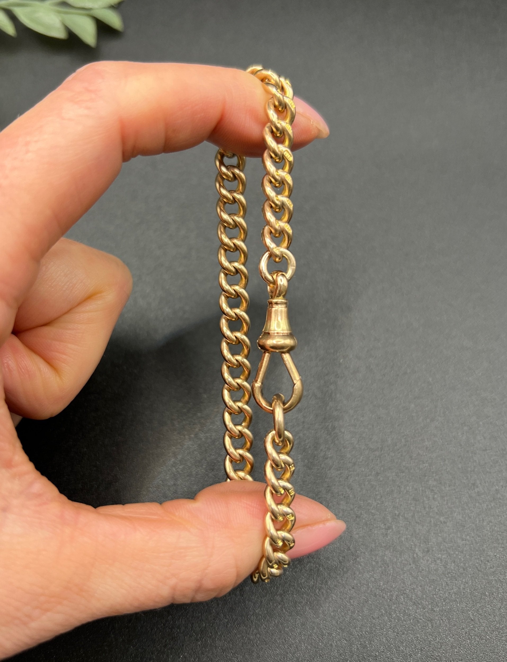 A gold curb link bracelet with a lobster claw clasp, held in a hand