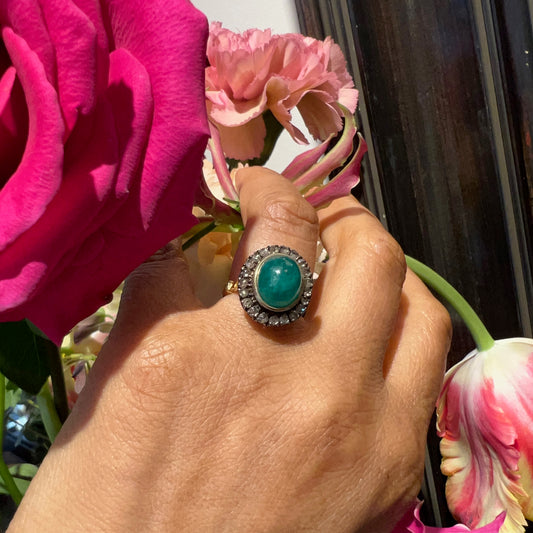 An oval emerald and diamond cluster ring in yellow gold and silver, modelled on a hand, with flowers