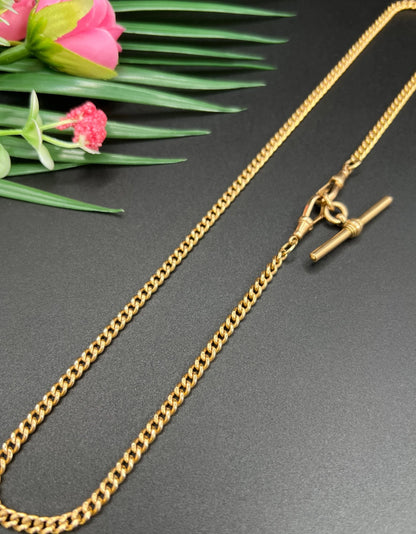 A gold curb link Albert chain, laid flat on a black background