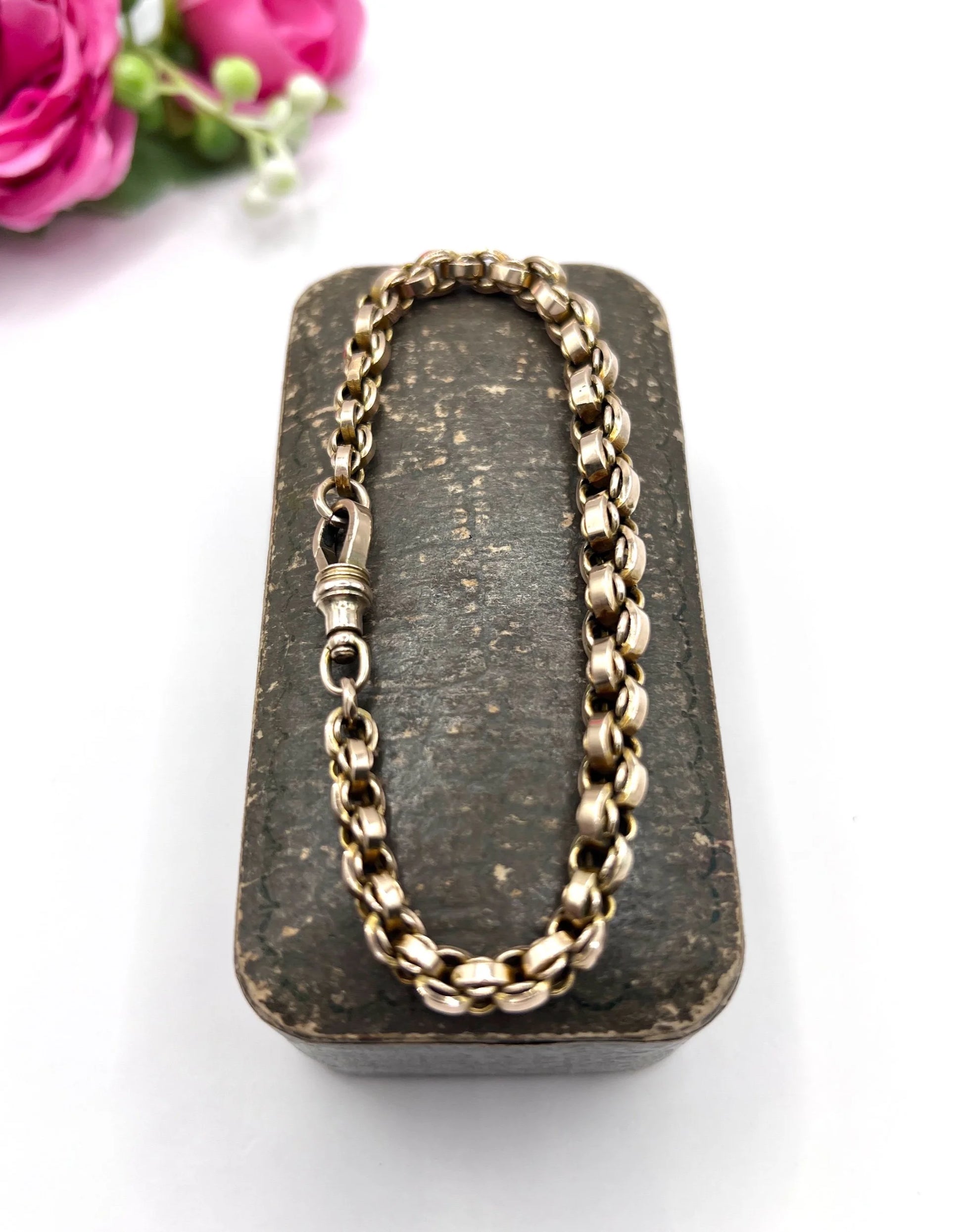 A gold round link bracelet with a lobster claw clasp, on an antique box