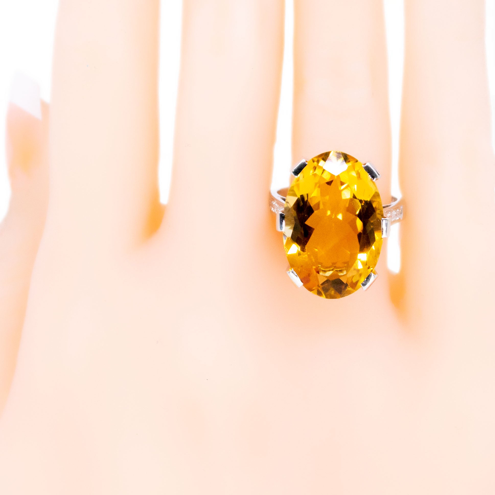 A large statement ring featuring an oval citrine with diamond shoulders in white gold, modelled on a hand