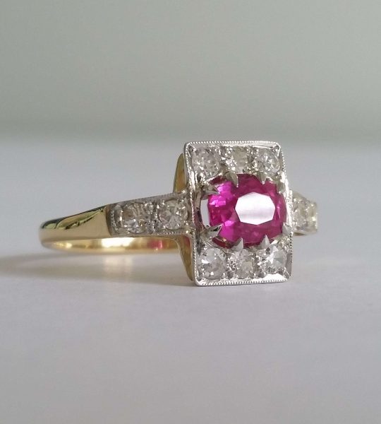 Art Deco Pink Sapphire and Old Cut Diamond Cluster Ring; an oval pink sapphire of intense colour is set in 18ct gold and platinum surrounded by small old cut diamonds. Circa 1920s