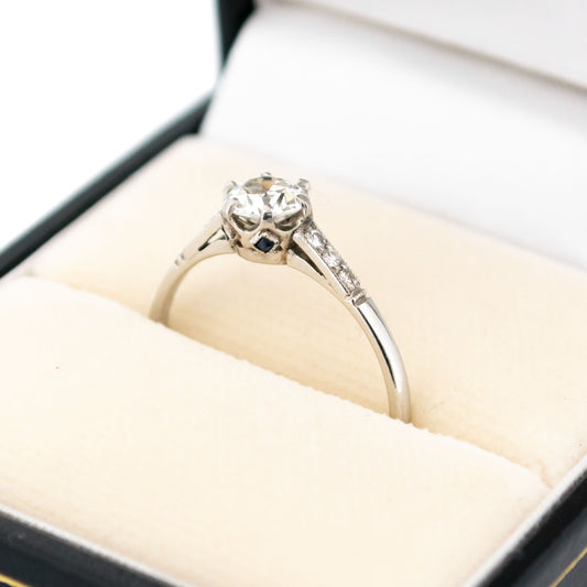 A platinum diamond ring with diamond shoulders and sapphire details, in a ring box