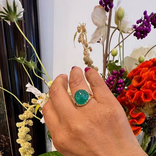 A solitaire cabochon cut emerald ring in yellow gold, modelled on a hand