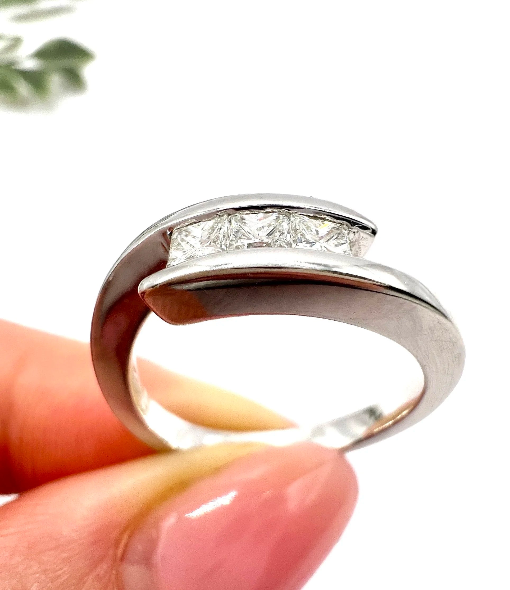 A three stone princess cut diamond crossover ring in white gold, held in a hand