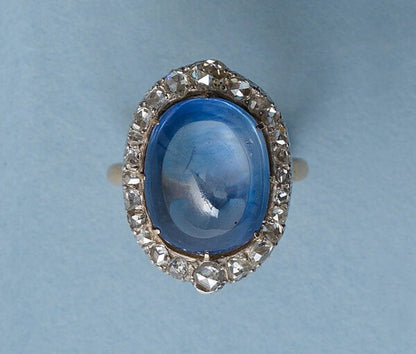 Antique Edwardian Cabochon Cut Sapphire and Diamond Oval Cluster Ring; 16.00 carat oval-cabochon cut sapphire surrounded by rose-cut diamonds, in silver and 18ct yellow gold, Circa 1910