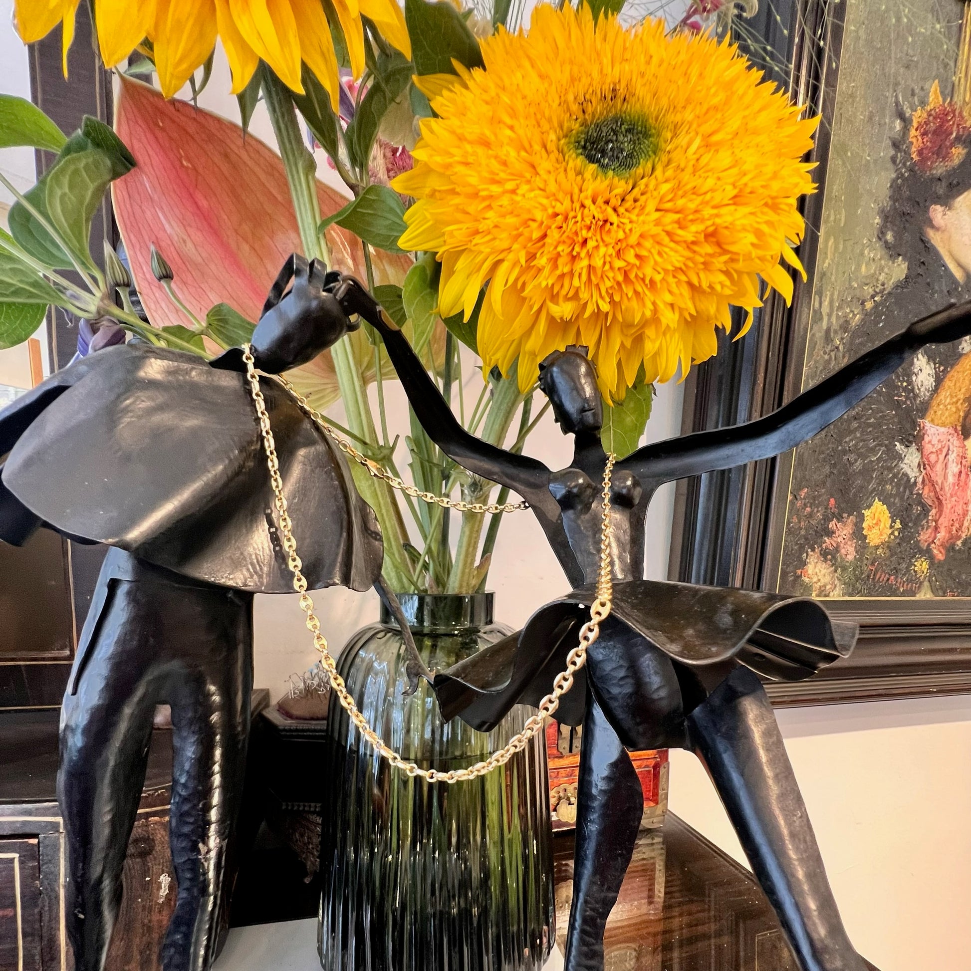 A yellow gold mariner link chain necklace, hanging over a statue and flowers