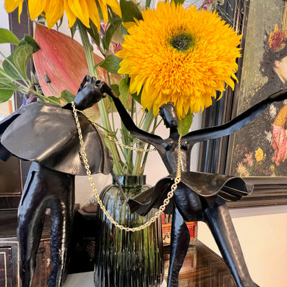 A yellow gold mariner link chain necklace, hanging over a statue and flowers