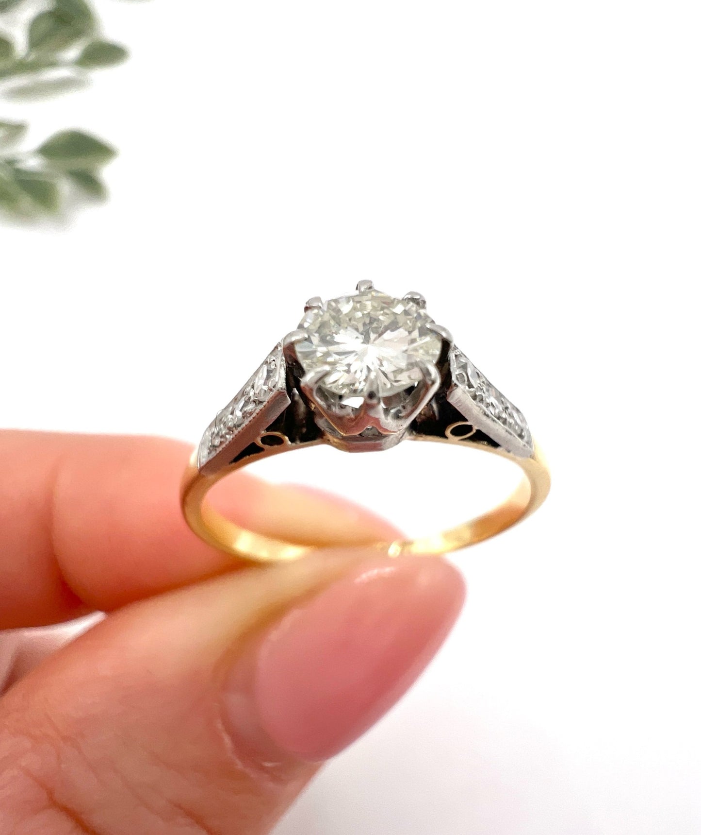 A diamond engagement style ring in yellow gold and platinum, held in a hand