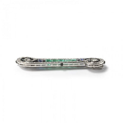 Art Deco French Emerald Sapphire Onyx and Diamond Bar Brooch in Platinum; set with 2.00cts calibre-cut emeralds, 0.50cts calibre-cut sapphires and fancy-cut black onyx, framed by 2.50cts old-cut and single-cut diamonds, in a scroll design, with enamelled detail