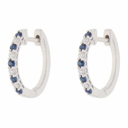 A pair of white gold hoop earrings set with round sapphires and diamonds, on a white background