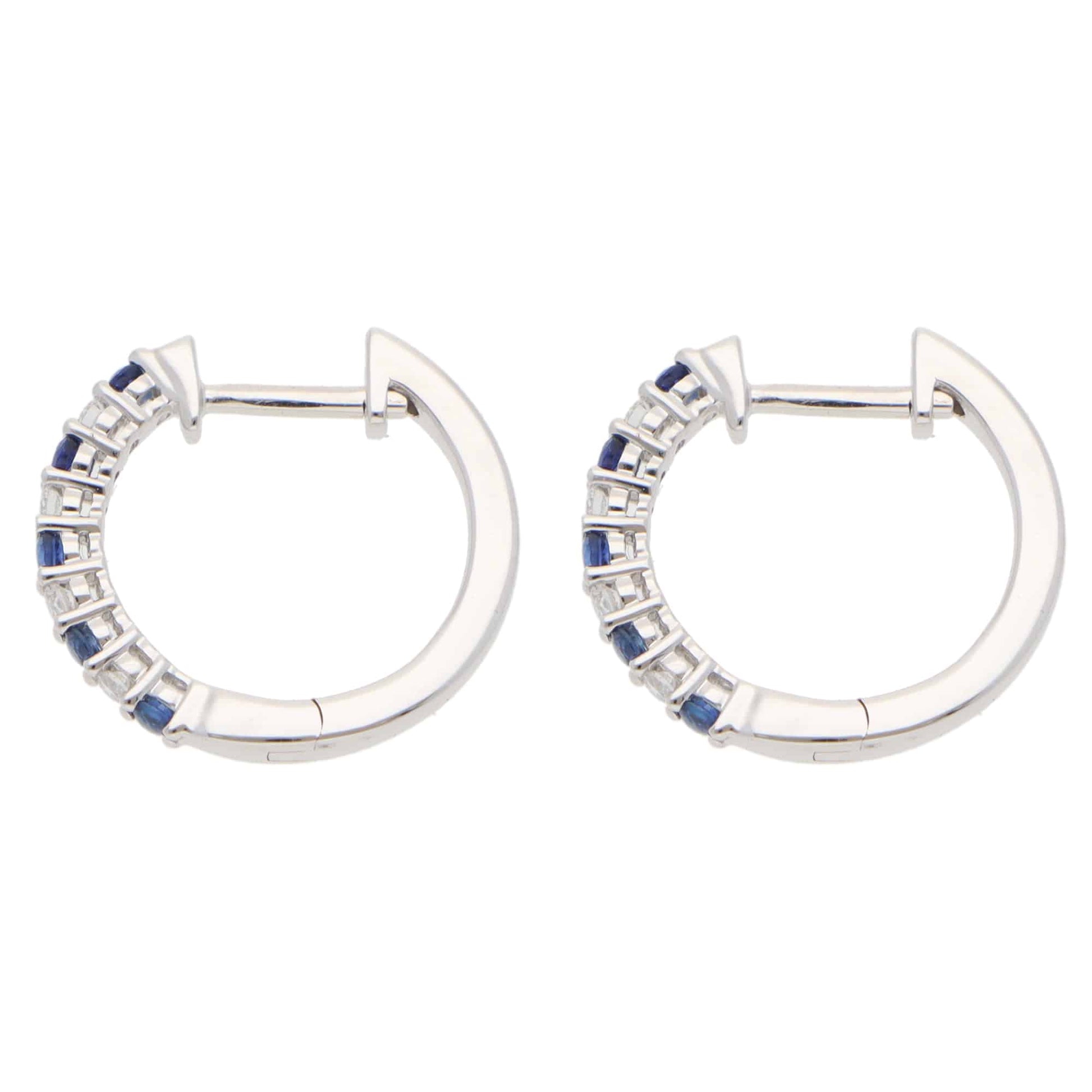 A pair of white gold hoop earrings set with round sapphires and diamonds, on a white background