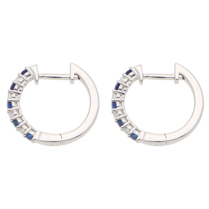 A pair of white gold hoop earrings set with round sapphires and diamonds, on a white background
