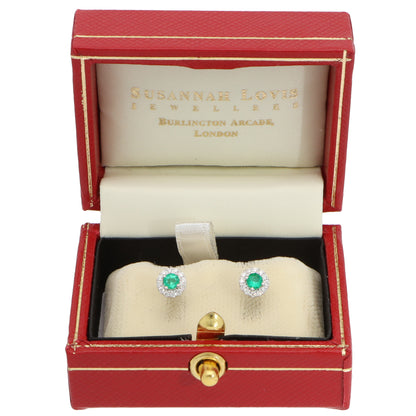 A pair of emerald and diamond round cluster stud earrings in white gold, in a red earring box, on a white background