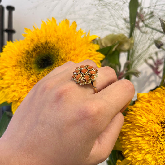 A yellow gold and coral flower design cluster ring, modelled on a hand