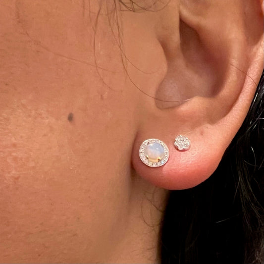 A round opal and diamond cluster stud earring modelled in an ear, with a diamond stud
