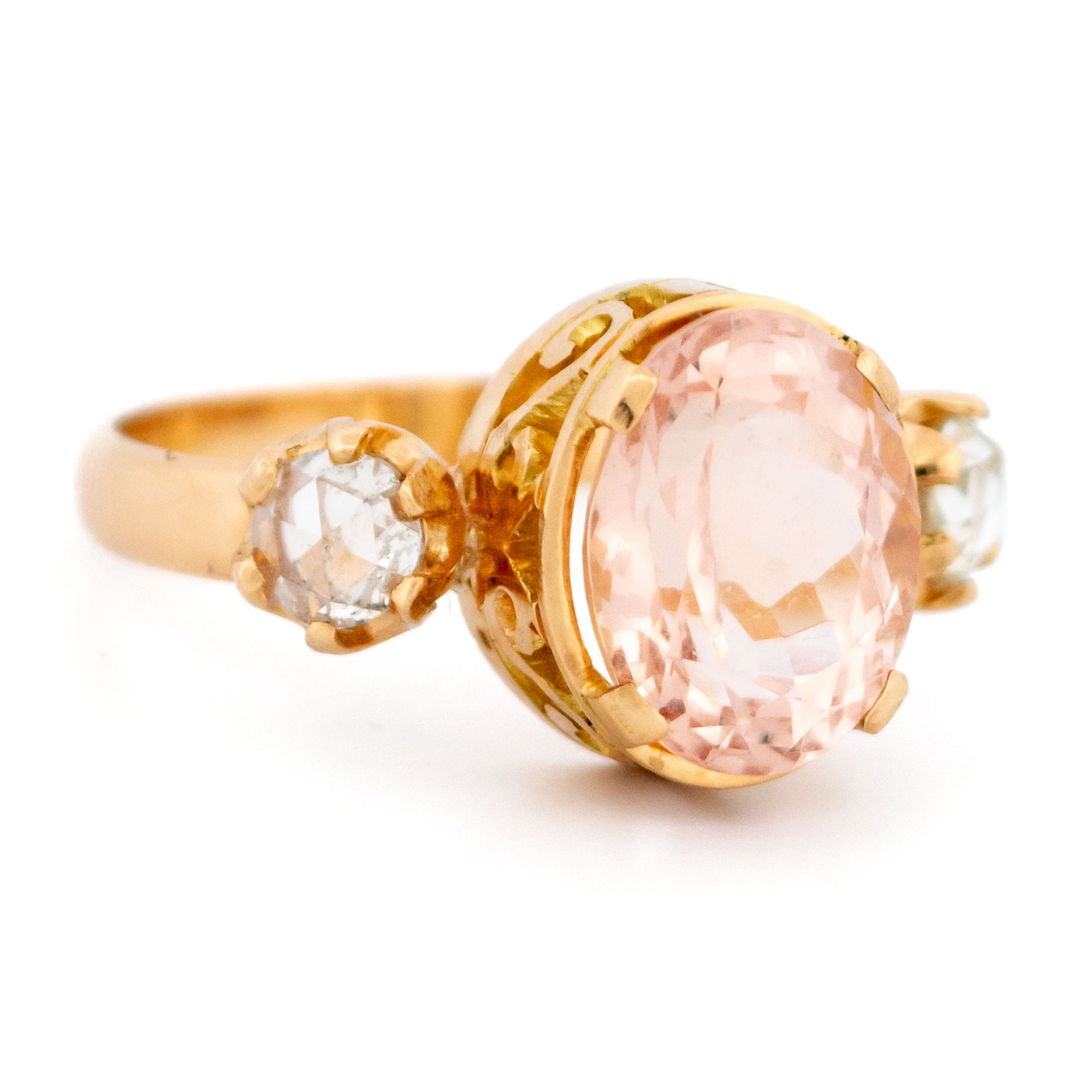 A three stone oval morganite and diamond ring in yellow gold, on a white background