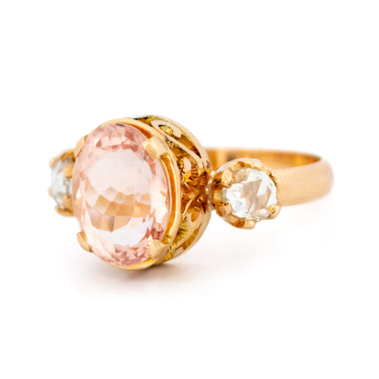 A three stone oval morganite and diamond ring in yellow gold, on a white background