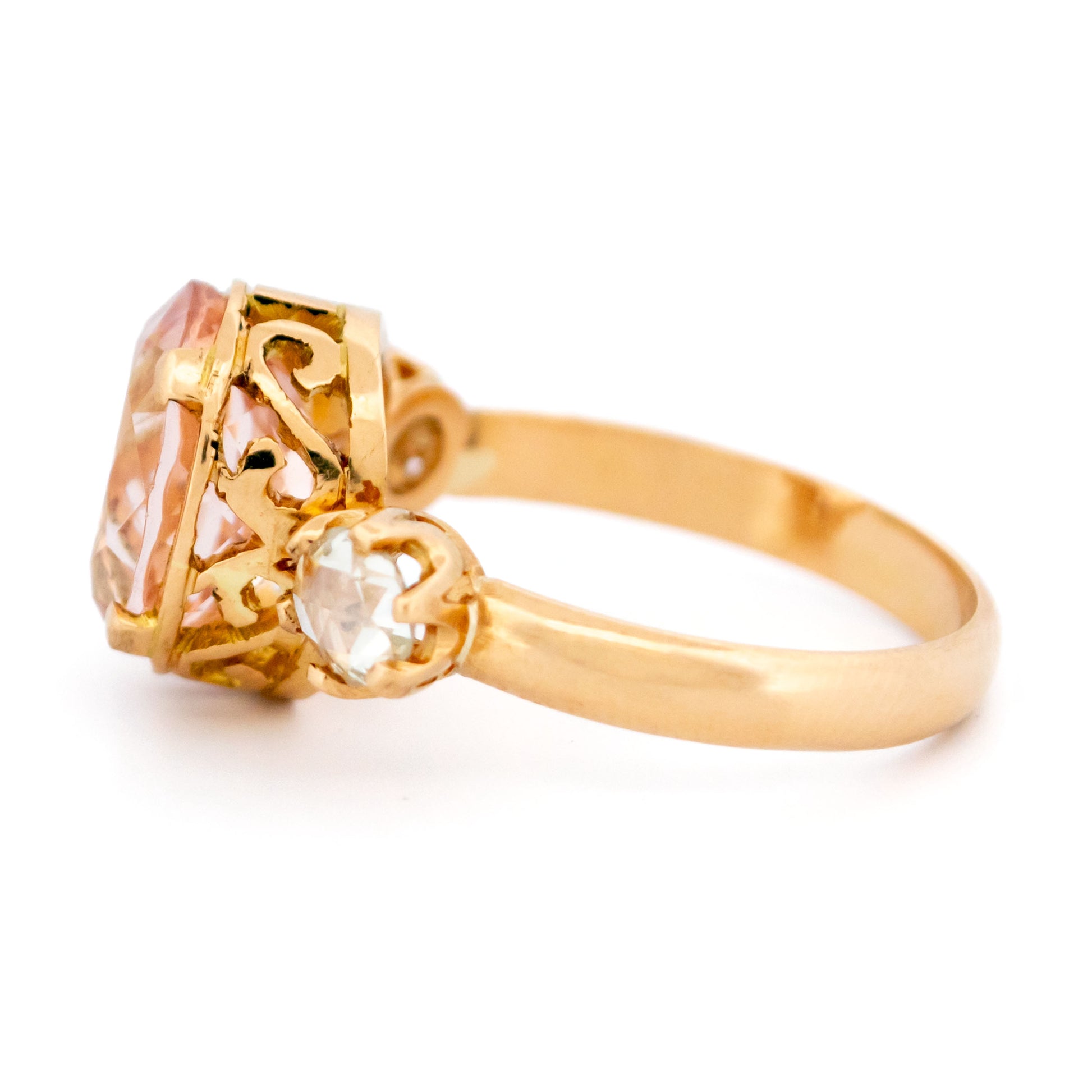 A three stone oval morganite and diamond ring in yellow gold, on a white background
