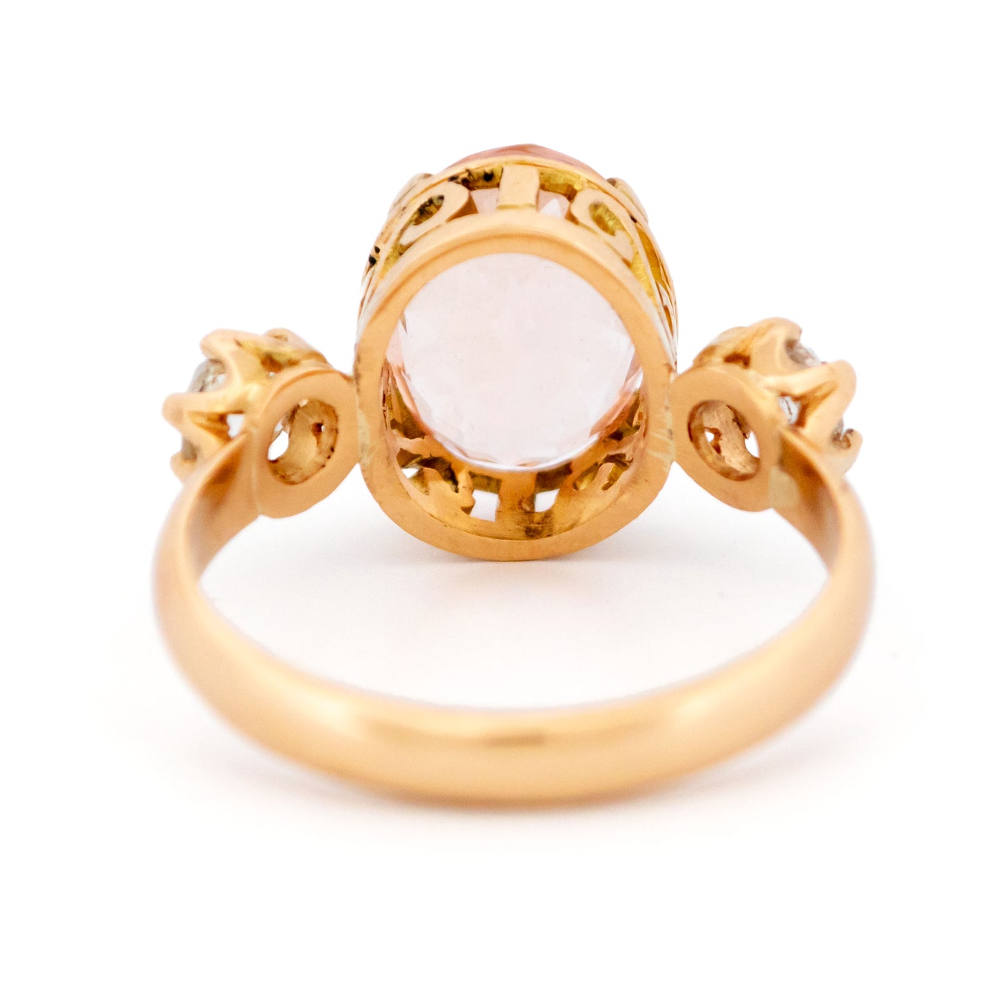 A three stone oval morganite and diamond ring in yellow gold, on a white background