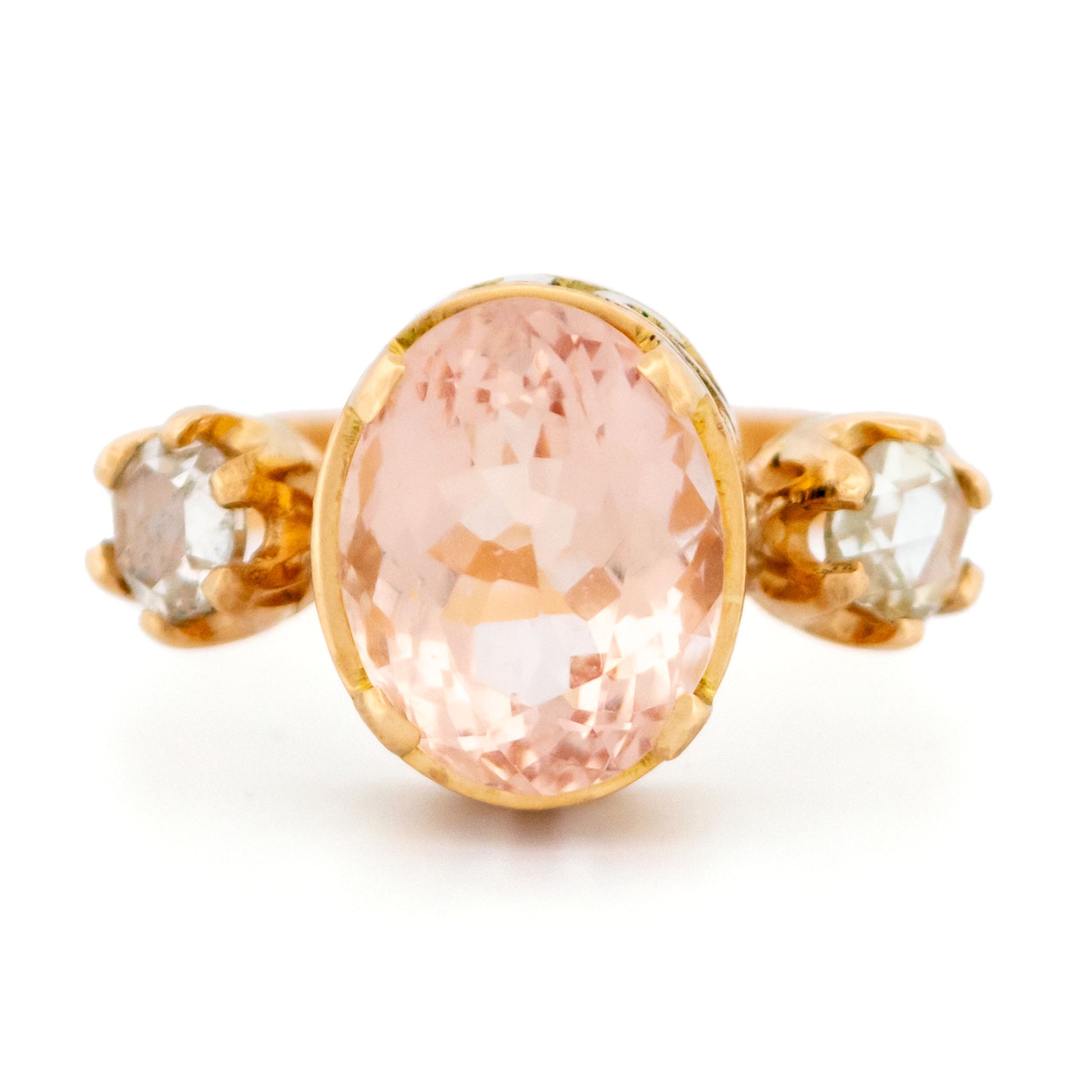 A three stone oval morganite and diamond ring in yellow gold, on a white background
